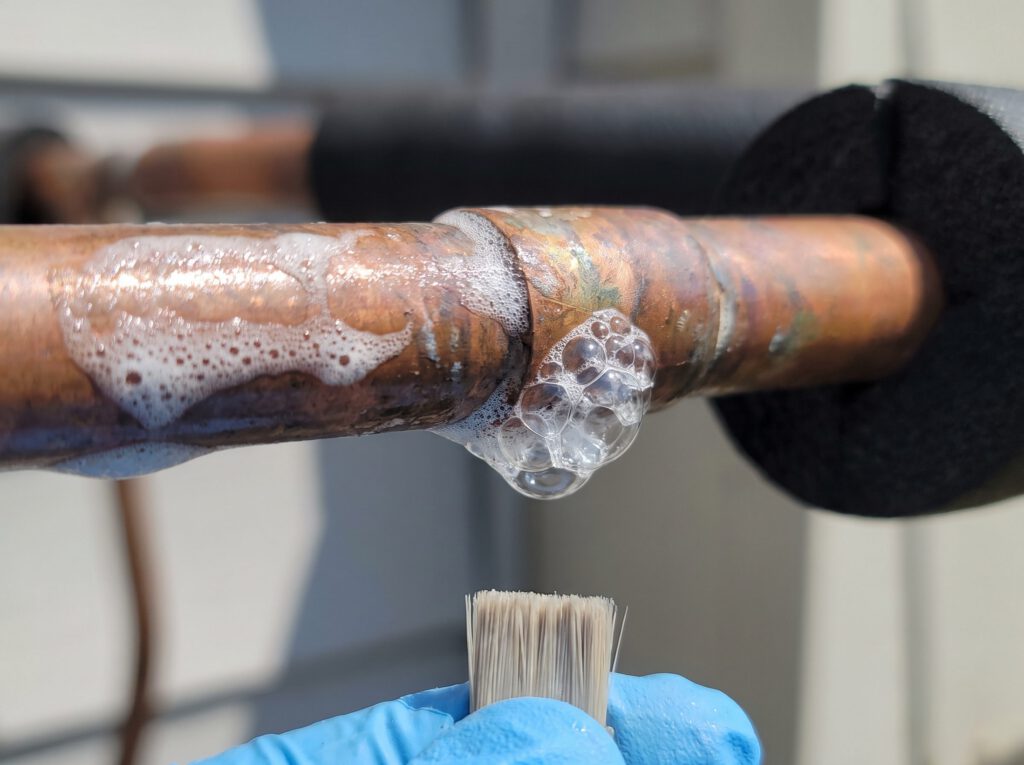 Soap bubbles forming on a brazed copper refrigerant line joint during a leak test
