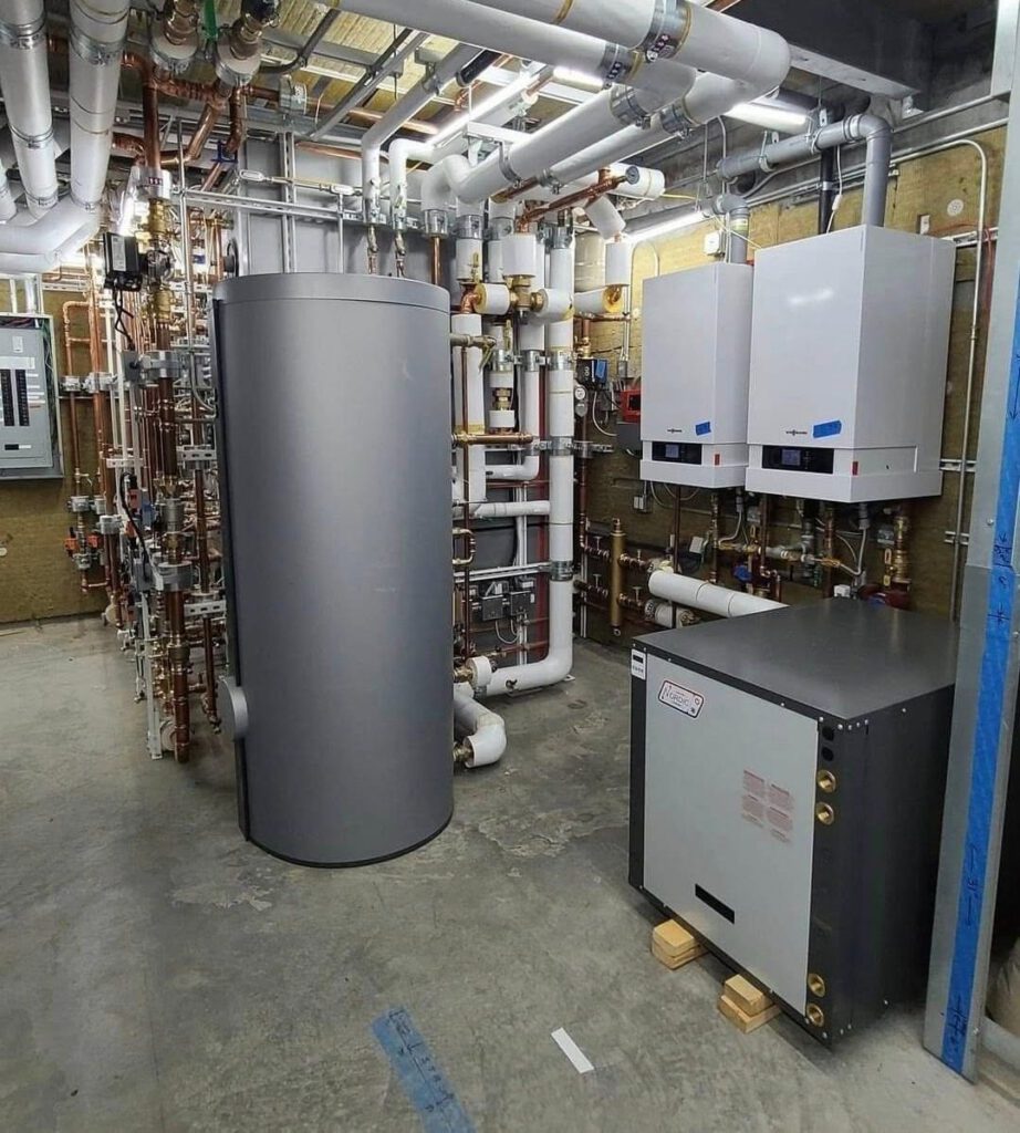 Commercial boiler room with a storage tank, two wall-hung boilers and insulated piping, installed by K&G Builders HVAC
