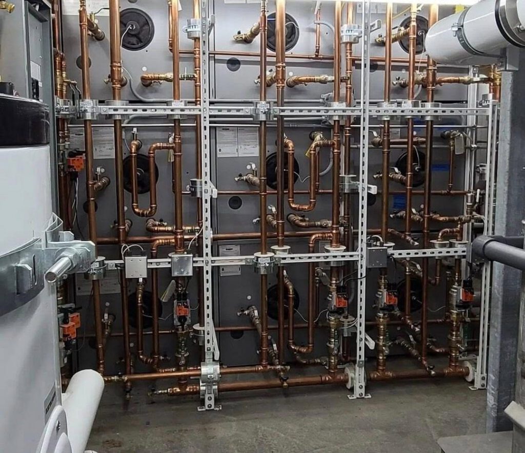 Copper piping manifold with pumps and valves on steel strut racks in a commercial mechanical room installed by K&G Builders HVAC